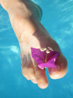 pied nu orné d'une fleur rose entre les orteils au-dessus d'une eau bleue cristalline