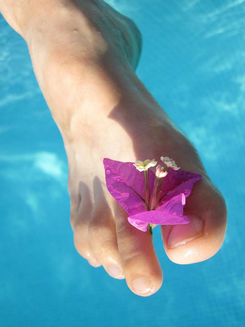 Pied nu fleur entre les orteils au-dessus d'une eau bleuc cristalline